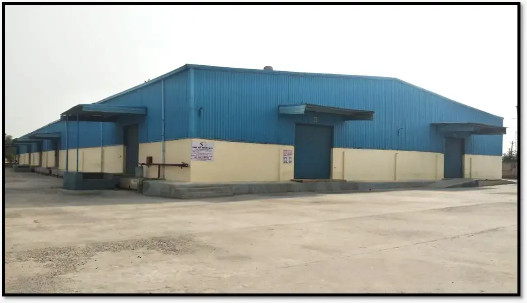 Exterior view of a blue and cream industrial warehouse with loading doors and a concrete yard.