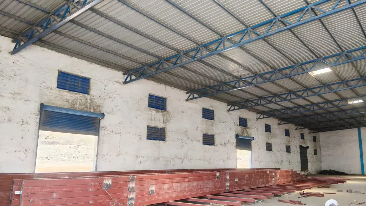 Warehouse interior with corrugated roof, blue steel trusses, white walls, shutter openings, and a raised brick loading platform.