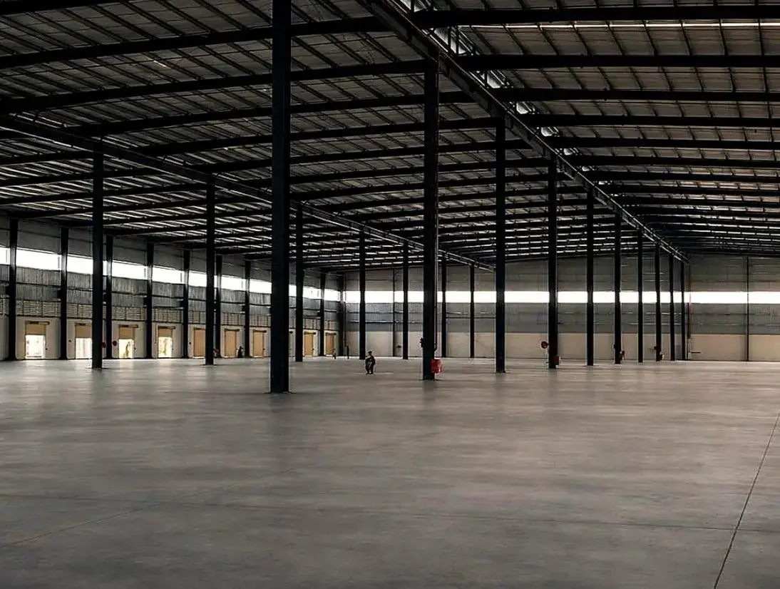 Large empty warehouse interior with concrete floor, steel columns, and corrugated metal roof.